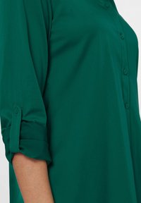 Groene overhemd met knopen, gemaakt van gladde stof, met opgerolde mouwen en knoopdetails aan de voorkant, met een eenvoudig en klassiek ontwerp.