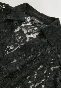 Black lace blouse with a collar, featuring a floral pattern and sheer texture. Label reads "NEXT." Fabric has intricate detailing.