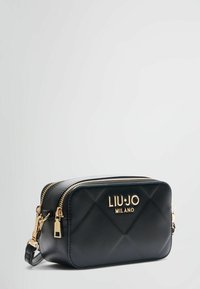 Crna kožna crossbody torba s kvadratnim dizajnom, zlatnim hardverom, dvostrukim zatvaračem i ugraviranim logotipom na prednjoj strani. Kompaktna i strukturirana forma.