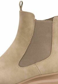 Bottine beige avec un extérieur en cuir doux, des panneaux latéraux élastiques et une semelle en caoutchouc texturée. Coutures détaillées le long des bords.