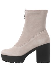 Beige mocka ankelsko med hög klack i blockformat och strukturerad svart plattform. Har en sidodragkedja för stängning och en slät yta.