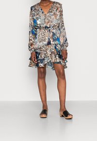 Robe à manches longues avec un motif floral et animalier coloré, col en V, ceinture à la taille et ourlet froncé. Associée à des sandales noires à enfiler.