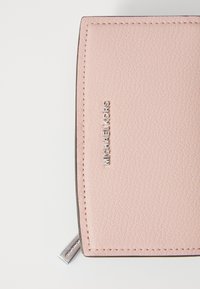 Portafoglio in pelle rosa con superficie testurizzata, con logo "Michael Kors" in argento e un piccolo tirazip in metallo. I bordi sono cuciti in modo ordinato.