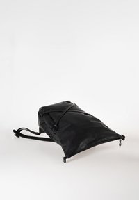 Zaino nero in pelle, dalla forma rettangolare, con spallacci regolabili, tasca laterale e chiusura con zip, arricchito da cinghie decorative sulla parte frontale.