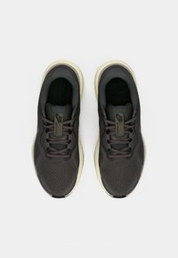 Un paio di scarpe da corsa grigio scuro con suole beige chiaro, lacci neri e tomaia in mesh, viste dall'alto su uno sfondo bianco.