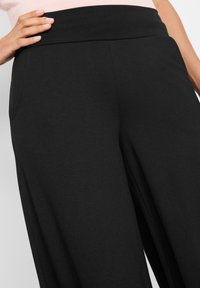 Pantaloni neri a gamba larga realizzati in tessuto morbido con una finitura liscia, dotati di una cintura spessa e tasche laterali.