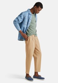 Camisa de mezclilla, camiseta verde, pantalones caqui y zapatos azules. Ajuste relajado con texturas y costuras notables en las prendas.