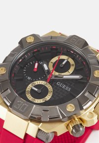 Schwarz Zifferblatt Uhr mit goldenen Akzenten, rotem Gummiband, strukturiertem Gehäuse und mehreren Unterdails. Verfügt über markante Stundenmarkierungen und Zeiger.