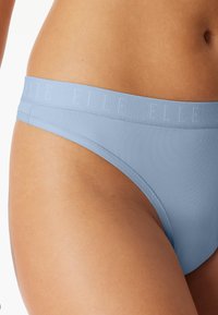 Světle modré spodní prádlo ve stylu bikiny s elastickým pasem, na kterém je vyražené jméno značky, zobrazující hladký a bezešvý vzhled.