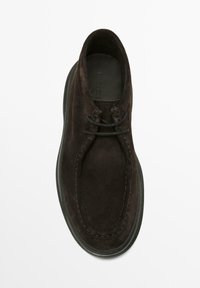 Brun ruskindsko med rund tå, snørefronter og en broderet design. Har en flad gummisål og en glat inderside.