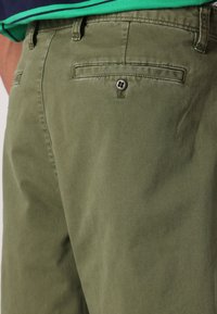 Olivgrüne Hosen aus weicher Baumwolle, mit einer Gesäßtasche und einem runden Knopf sowie subtiler Textur. Sauberes, maßgeschneidertes Design.