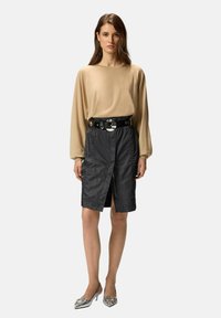 Haut beige à manches longues, jupe noire zippée avec fente à l'avant, boucle de ceinture circulaire argentée et chaussures à talons argentées. Textures de tissu lisses.