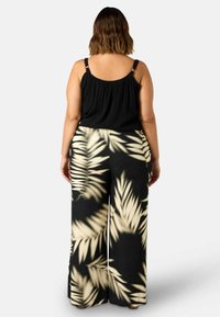 Top nero senza maniche con tessuto testurizzato; pantaloni a gamba larga con un motivo di foglie di palma crema su sfondo nero.