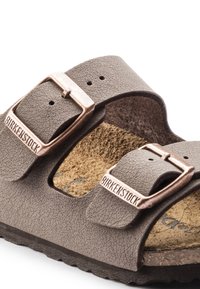 Barna Birkenstock szandál állítható, dupla csatos kialakítással, puha textúrájú felsőrész anyaggal és parafa talppal a kényelem érdekében.