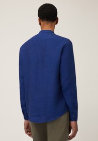 Blauwe linnen blouse met lange mouwen, een gebogen zoom, knoopmanchetten en een eenvoudige kraag, die een textuurstof toont.