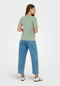 Lys grøn t-shirt med korte ærmer, parret med løse blå jeans og hvide sneakers. Stoffet ser blødt ud med et simpelt design og klassisk pasform.