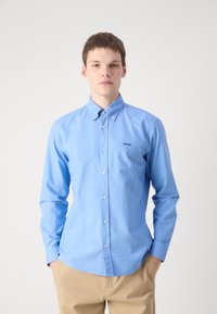 Lichtblauw overhemd met kraag, voorzien van een klein zwart logo op de borst, gemaakt van een zachte katoenstof, gecombineerd met beige broek.
