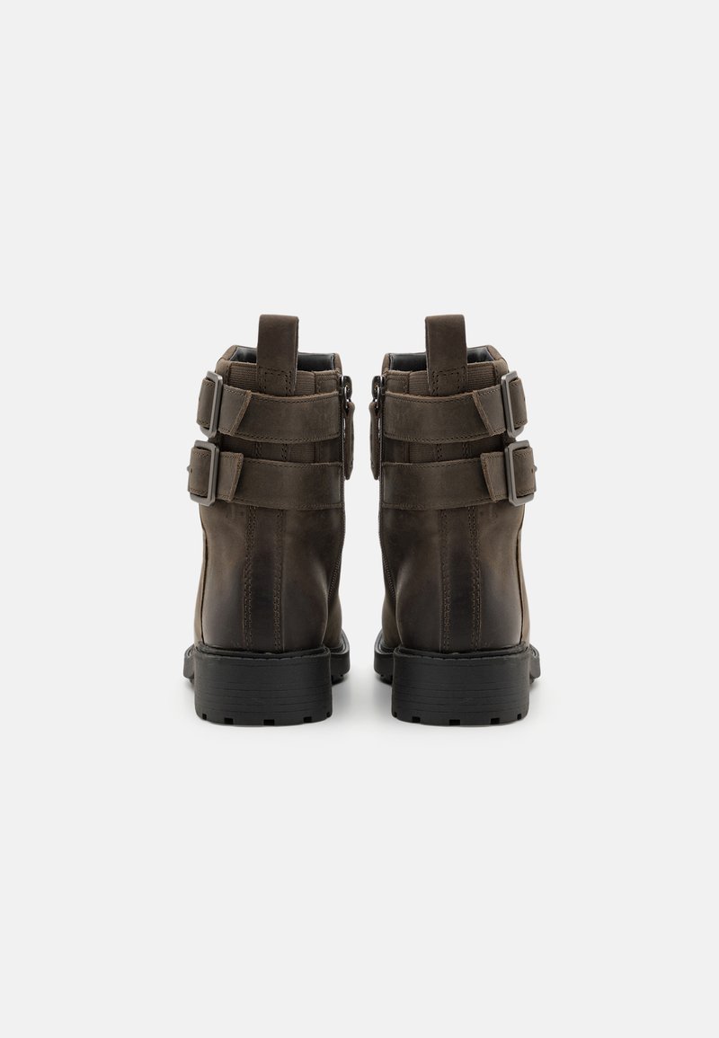 Botas de tobillo de cuero marrón con acentos de doble hebilla, un acabado texturizado y suelas de goma resistentes, con una altura que cubre el tobillo.