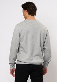 Grijze sweater met ronde hals en lange mouwen, gemaakt van zachte stof. De onderrand en de mouwen zijn ribbelig. Gekleed met zwarte broeken, gezien van achteren.