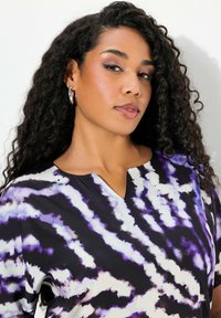 Blusa de cuello en V en tela ligera con un patrón de teñido anudado en tonos de púrpura, negro y blanco. Mangas cortas con un ajuste relajado.