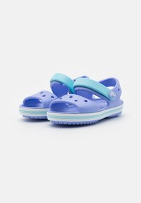 Purple rubber sandals featuring adjustable light blue straps, open-toe design, drainage holes, and a textured sole with a white-blue stripe.