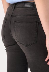 Mustat farkut, joissa on kapea malli, taka-taskut, hienovaraiset ompelut yksityiskohdat ja sileä pinta. Nahkainen logo-patch vyötäröllä.