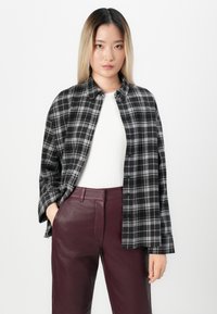 Zwart-wit geblokte blouse met een knoopsluiting, lange mouwen en een ontspannen pasvorm, gedragen over een wit topje en bordeauxleren broek.