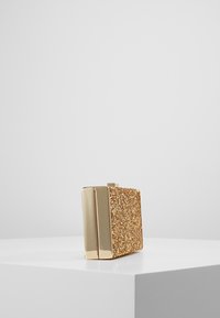 Złota kopertówka z brokatem o prostokątnym kształcie, z błyszczącymi złotymi okuciami, gładką fakturą i bezpiecznym zamknięciem zatrzaskowym na górze.