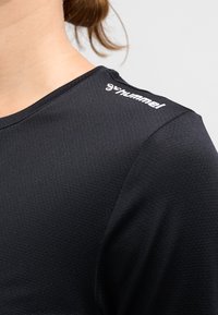 Czarna sportowa koszulka z teksturowanej tkaniny z okrągłym dekoltem. Na ramieniu znajduje się biały logo "hummel".