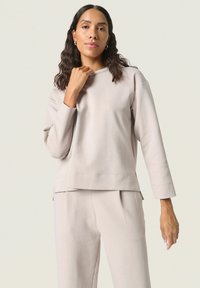 Lys beige sweatshirt med lange ærmer og en afslappet pasform. Har en rund halsudskæring og sideslids ved kanten. Glat, blød stofstruktur.