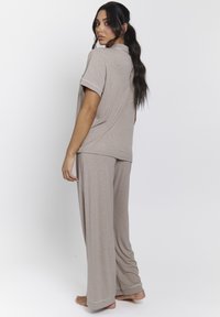 Conjunto de pijama beige con una parte superior de manga corta y pantalones de pierna ancha, que presenta una tela texturizada y ribetes blancos en los bordes.
