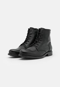 Botas negras de cuero hasta el tobillo con una textura suave, puntera redonda y diseño de cordones. Presentan un tacón bajo apilado y detalles de costura mínimos.