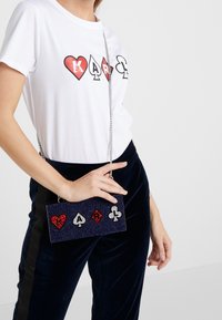 Navy glitter clutch bag with red and silver card suit appliqués, silver chain strap, rectangular shape, and smooth texture, held in hand.