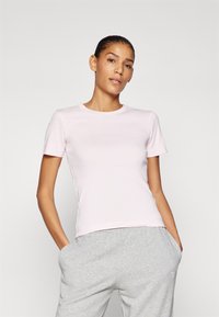 Růžové krátké tričko s kruhovým výstřihem vyrobené z bavlny, se slim fit střihem, kombinované se šedými tepláky. Hladká textura, bez viditelných vzorů.
