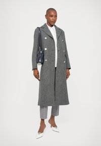 Gray wool blend overcoat with a double-breasted design, large silver buttons, and notched lapels. White shirt, checkered trousers, and white heels.