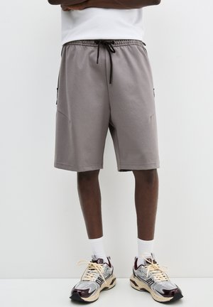 Pantaloni sportivi grigi chiari realizzati in tessuto morbido, con una vita elasticizzata dotata di cordoncino e tasche laterali.