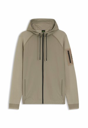 Beige gewatteerde jas met capuchon, zwarte rits over de hele voorkant, capuchon met trekkoord, geribbelde mouwen, zijzakken en een zak met rits op de linker bovenarm.