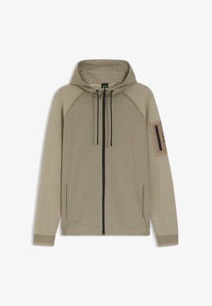 Beige gewatteerde jas met capuchon, zwarte rits over de hele voorkant, capuchon met trekkoord, geribbelde mouwen, zijzakken en een zak met rits op de linker bovenarm.