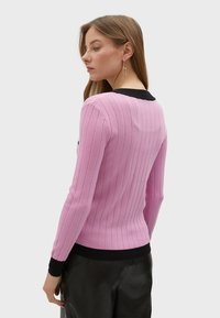 Rosa ribbad tröja med långa ärmar och svart kant vid kragen och muddarna, som har subtil vertikal textur och figurnära design.