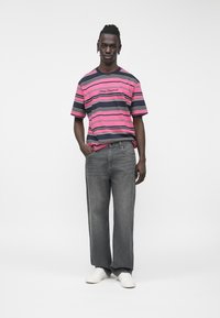 T-shirt à manches courtes rayé rose et marine avec un logo poitrine, associé à un jean gris à jambes larges et des baskets blanches. Texture de tissu lisse.