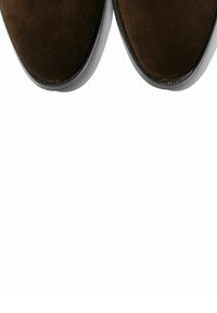 Scarpe in suede marrone con punta rotonda, dotate di una suola in gomma bianca a contrasto e cuciture lungo il bordo per un tocco di dettaglio.