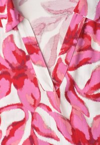 Cuello y escote en V de una prenda con un audaz patrón floral abstracto en rosa, rojo y blanco sobre tela ligera.