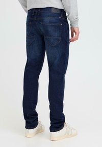 Jeans de mezclilla azul oscuro con corte recto y un ligero desgaste. Presentan dos bolsillos traseros con detalles de costura y una pequeña etiqueta de la marca en la cintura.