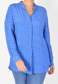 Blå långärmad skjorta med V-ringning, prydd med vita prickar och knappade muddar. Mjuk tygkvalitet med en lös passform.
