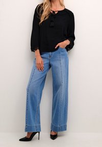 Svart blus med nyckelhålsutskärning, tofsdetaljer och spetsärmar, i kombination med vidbeniga ljusblå jeans med vikta fållar och sydda detaljer.