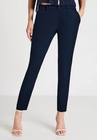 Pantalons ajustés navy en tissu lisse avec poches et passants de ceinture. Présente un design épuré et taillé avec une légère élasticité.