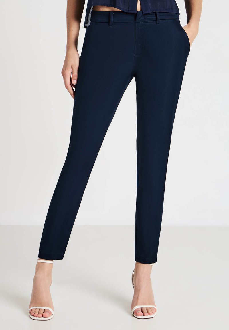 Pantalons ajustés navy en tissu lisse avec poches et passants de ceinture. Présente un design épuré et taillé avec une légère élasticité.