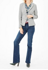 Blazer grigio aderente sopra una camicetta floreale, abbinato a jeans a zampa d'elefante blu scuro e tacchi verdi. Tessuto liscio con un design strutturato.