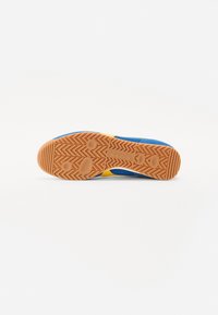 Sula av blå och gula sportskor med gummigummi som har fiskbensmönster och cirkulära grepp på vit bakgrund.