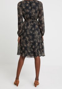 Svart klänning med långa ärmar, åtdragen midja och knäslängd fåll. Har ett spritt mönster av guldprickar på lätt genomskinligt tyg.